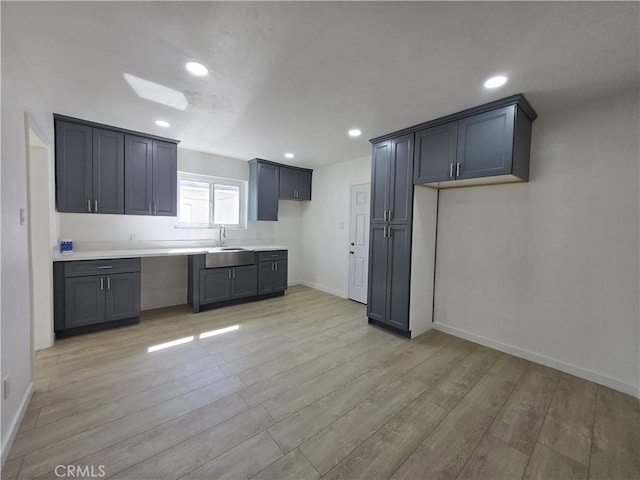 kitchen featuring baseboards, light countertops, light wood-style floors, a sink, and recessed lighting