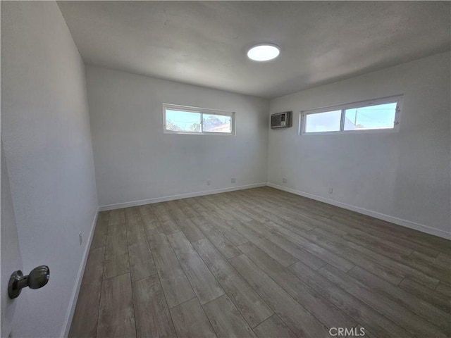 empty room featuring an AC wall unit, wood finished floors, a wealth of natural light, and baseboards