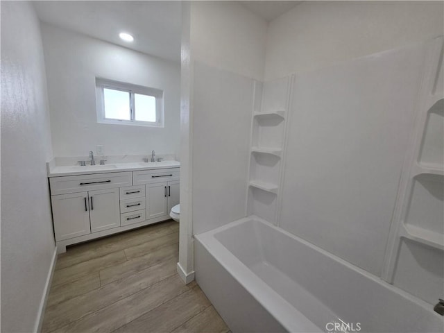 bathroom featuring toilet, a sink, double vanity, and wood finished floors