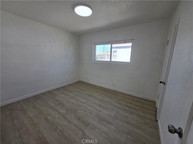 spare room with baseboards and wood finished floors