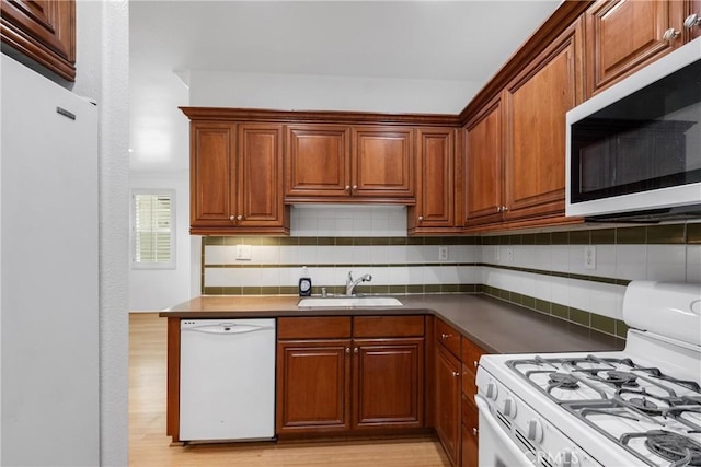 kitchen featuring light wood-style floors, white appliances, tasteful backsplash, a sink, and dark countertops