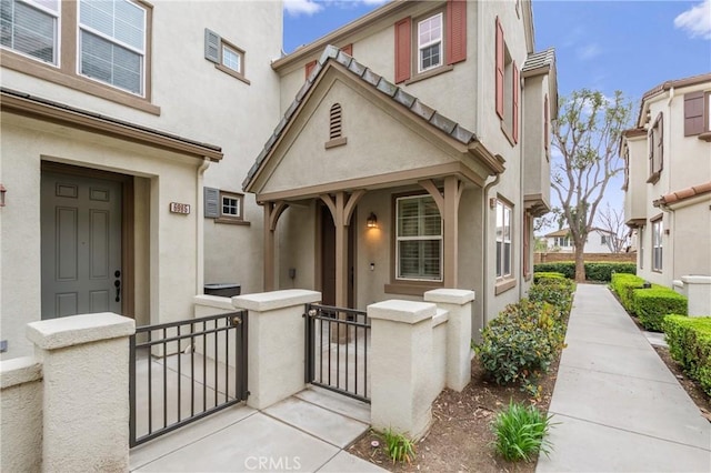 property entrance featuring covered porch, a gate, fence, and stucco siding