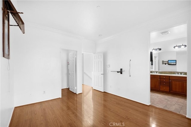 unfurnished bedroom with ensuite bath, ornamental molding, wood finished floors, a sink, and a walk in closet