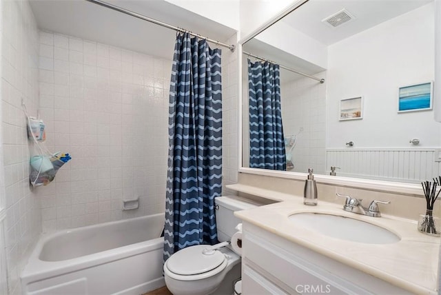 bathroom with visible vents, toilet, a wainscoted wall, shower / bath combo with shower curtain, and vanity