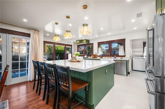 kitchen with stainless steel appliances, a spacious island, visible vents, light countertops, and green cabinetry