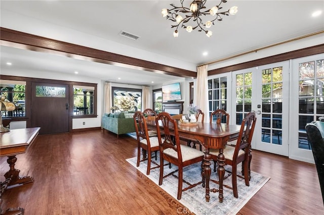 dining space with a notable chandelier, a fireplace, wood finished floors, visible vents, and french doors