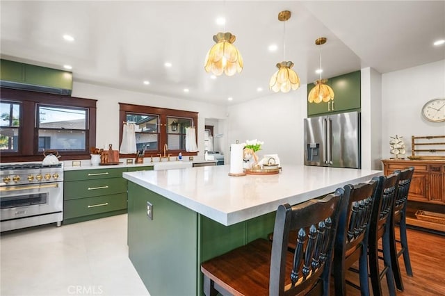 kitchen featuring premium appliances, light countertops, green cabinets, and a kitchen bar