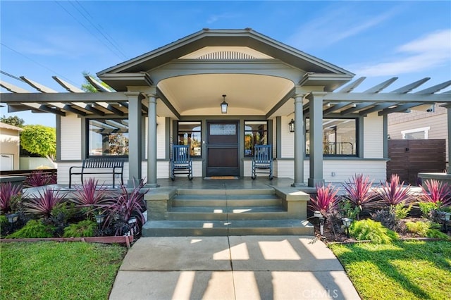 view of exterior entry featuring covered porch and a pergola