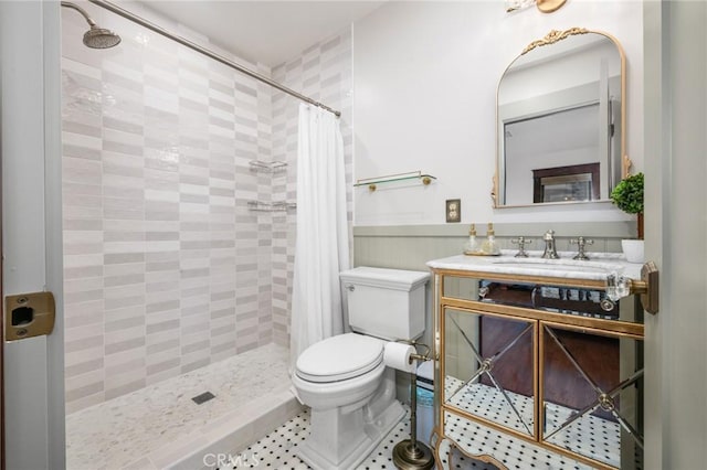 bathroom featuring a wainscoted wall, vanity, toilet, and tiled shower