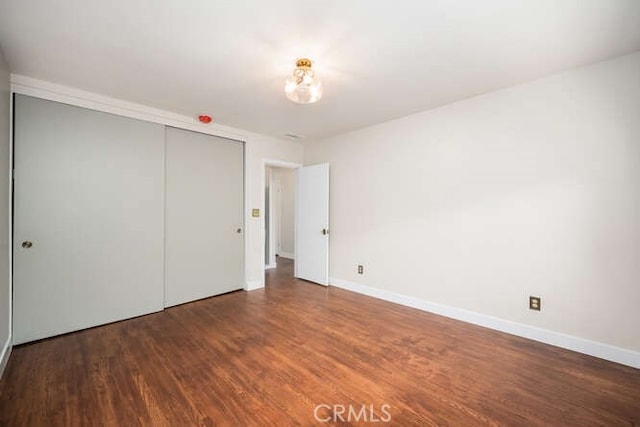 unfurnished bedroom featuring a closet, wood finished floors, and baseboards