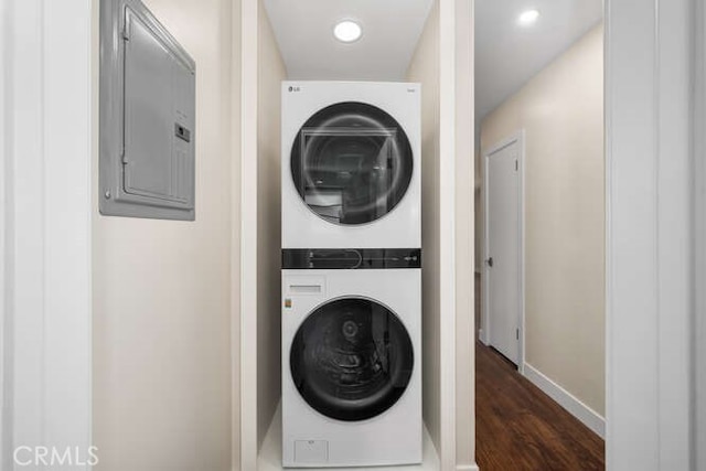 laundry area with dark wood-style floors, stacked washer and dryer, laundry area, electric panel, and baseboards