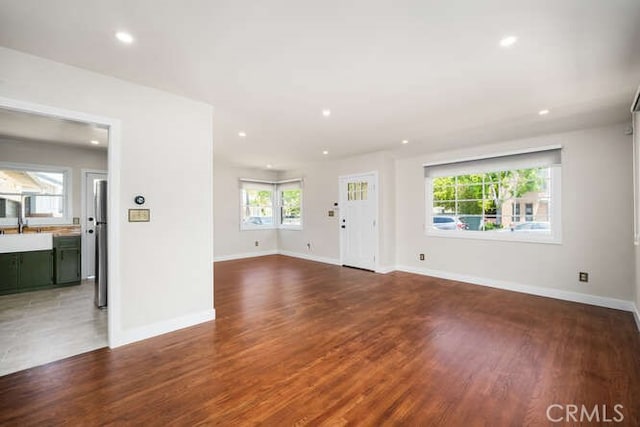 unfurnished living room with recessed lighting, a sink, baseboards, and wood finished floors