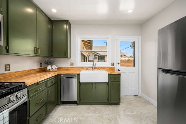 kitchen with butcher block countertops, a sink, baseboards, appliances with stainless steel finishes, and green cabinetry