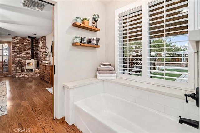 full bathroom with wood finished floors, visible vents, a wood stove, and a bath