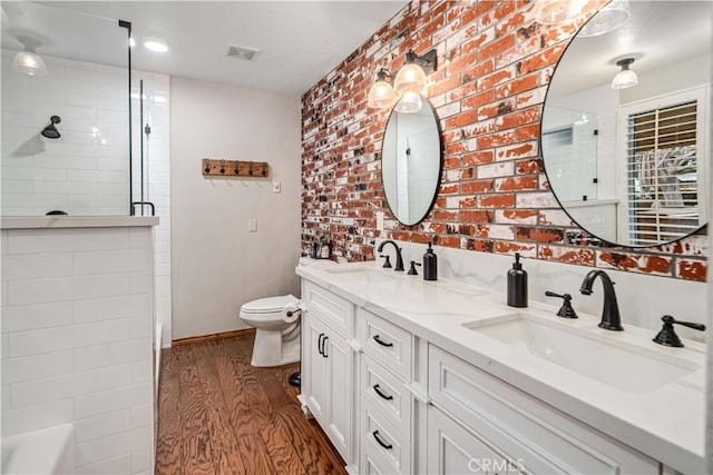 full bath featuring visible vents, a sink, a tile shower, and wood finished floors