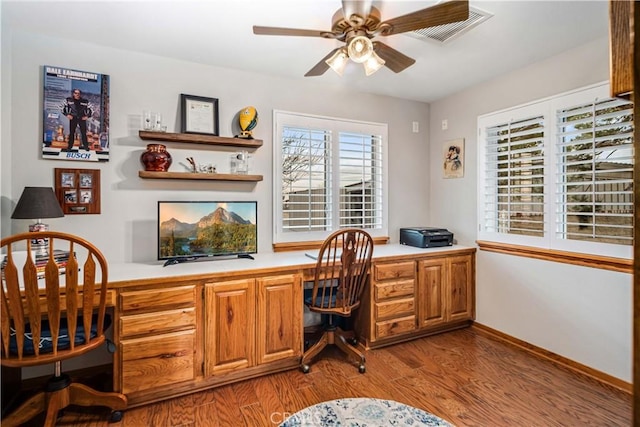 office area with wood finished floors, visible vents, baseboards, a ceiling fan, and built in desk