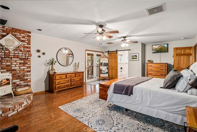 bedroom featuring a barn door, wood finished floors, visible vents, access to outside, and a wood stove