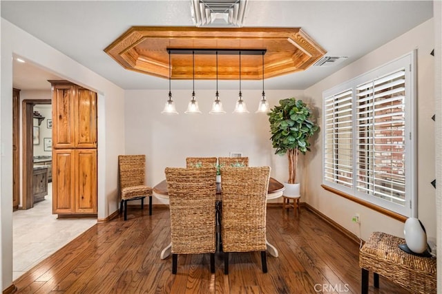 dining area with a raised ceiling, baseboards, visible vents, and hardwood / wood-style floors