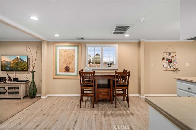 dining space with light wood finished floors, ornamental molding, and visible vents