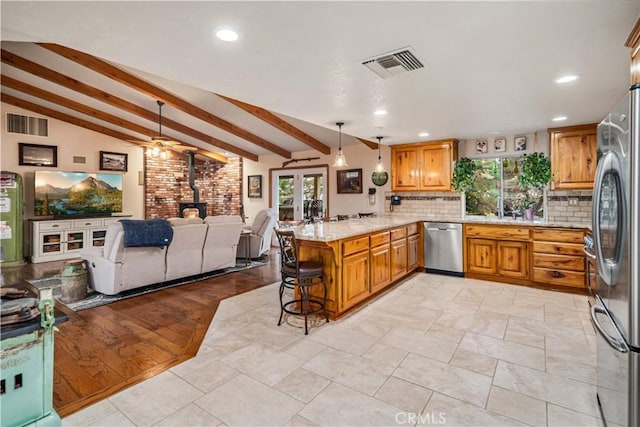 kitchen featuring visible vents, open floor plan, a wood stove, a peninsula, and stainless steel appliances