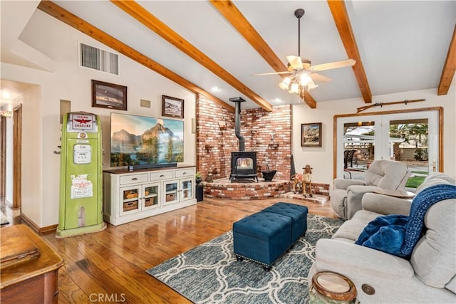 living room with vaulted ceiling with beams, visible vents, a wood stove, ceiling fan, and wood finished floors