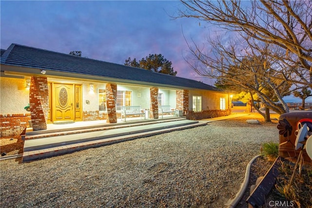 back of house at dusk featuring stucco siding and brick siding