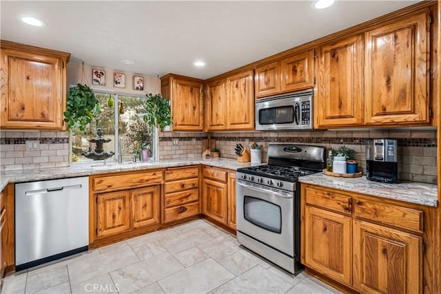 kitchen with light stone counters, a sink, appliances with stainless steel finishes, tasteful backsplash, and brown cabinetry