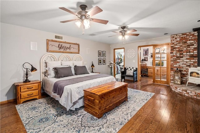 bedroom with dark wood-type flooring, a wood stove, visible vents, and a ceiling fan