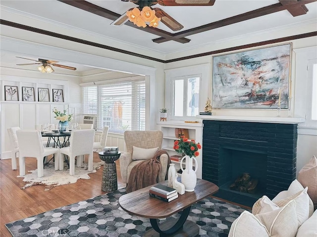 sitting room with a ceiling fan, a brick fireplace, crown molding, and wood finished floors