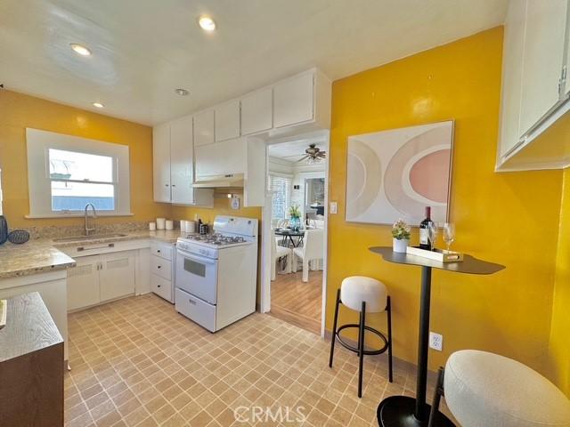 kitchen with under cabinet range hood, recessed lighting, white cabinets, and white gas stove