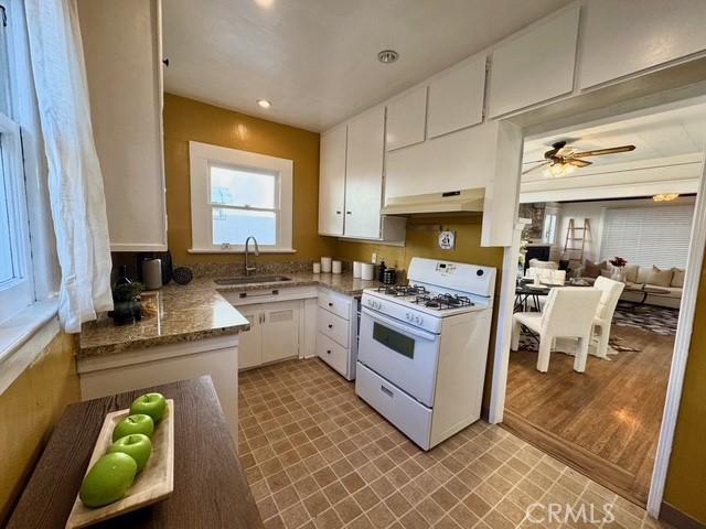 kitchen with white gas range, a sink, white cabinetry, and under cabinet range hood