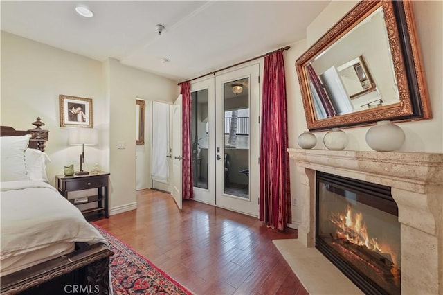 bedroom featuring baseboards, a premium fireplace, wood finished floors, access to outside, and french doors