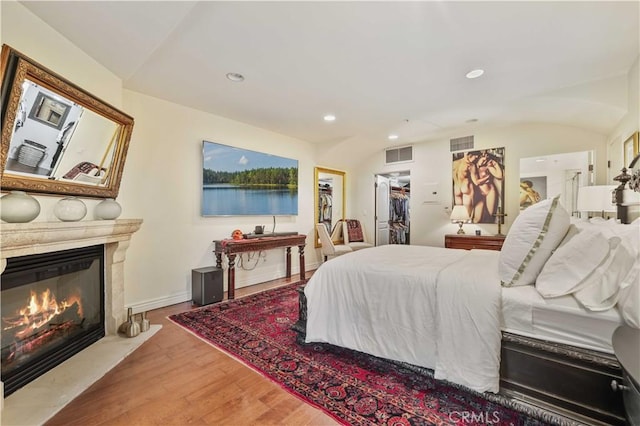 bedroom with a glass covered fireplace, wood finished floors, visible vents, and recessed lighting