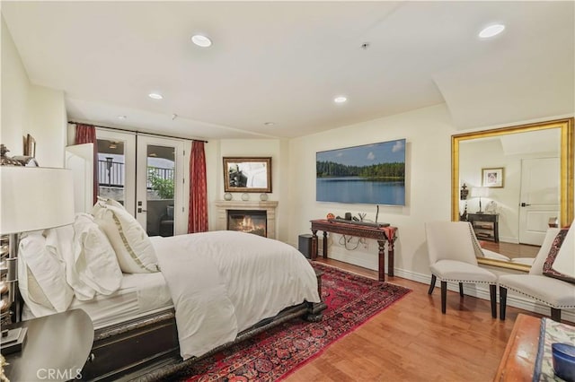 bedroom featuring a warm lit fireplace, wood finished floors, access to outside, french doors, and recessed lighting