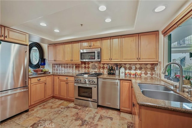 kitchen featuring dark stone counters, appliances with stainless steel finishes, a sink, a tray ceiling, and backsplash