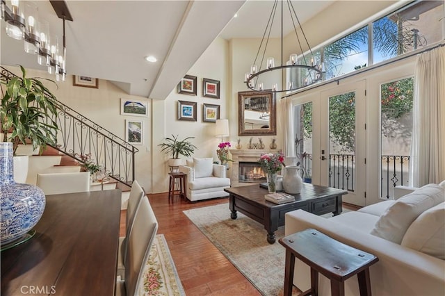 living room featuring a chandelier, a high ceiling, wood finished floors, a lit fireplace, and stairway