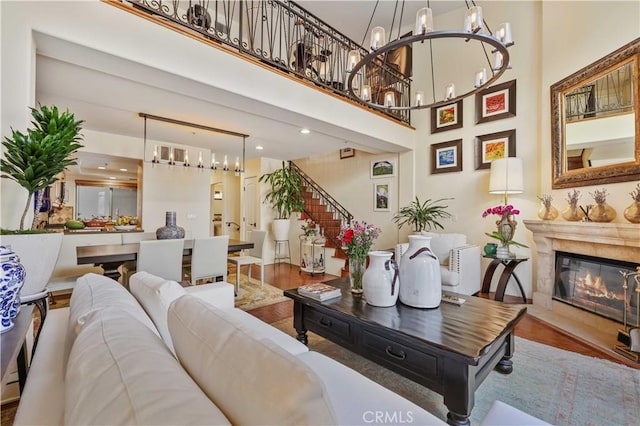 living area with a premium fireplace, wood finished floors, a towering ceiling, stairs, and an inviting chandelier