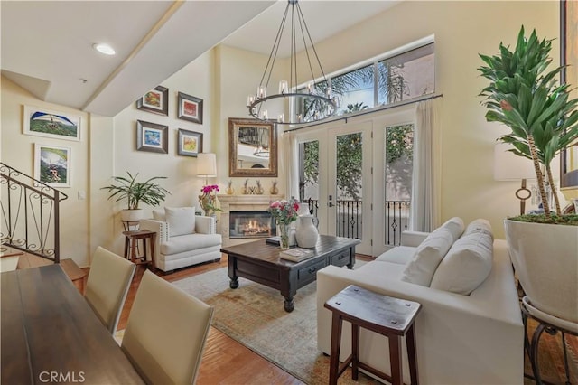 living area featuring a notable chandelier, wood finished floors, french doors, stairway, and a glass covered fireplace