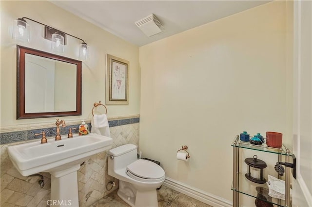 half bath featuring visible vents, wainscoting, toilet, tile patterned floors, and tile walls