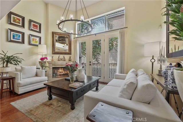 living room featuring french doors, a notable chandelier, a high ceiling, a glass covered fireplace, and wood finished floors