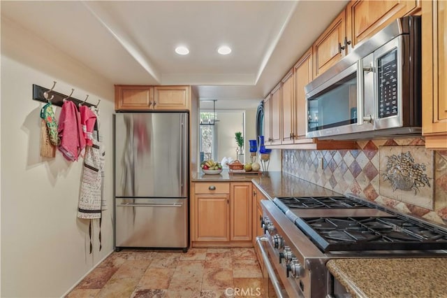 kitchen featuring stainless steel appliances, recessed lighting, a raised ceiling, decorative backsplash, and stone finish flooring