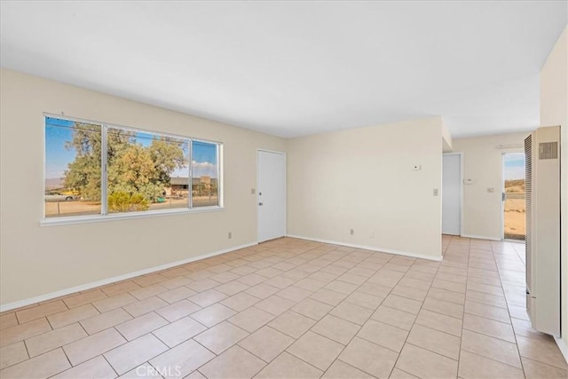 spare room with light tile patterned floors, a heating unit, and baseboards