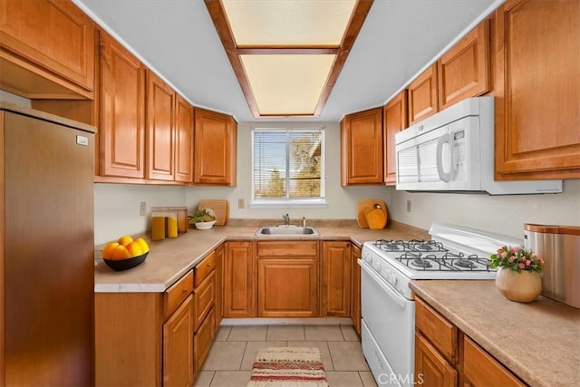 kitchen with light countertops, brown cabinets, light tile patterned flooring, white appliances, and a sink