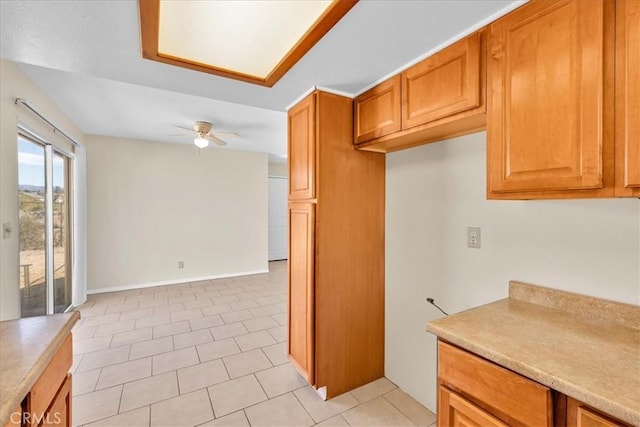 kitchen with baseboards, light tile patterned flooring, ceiling fan, light countertops, and brown cabinets