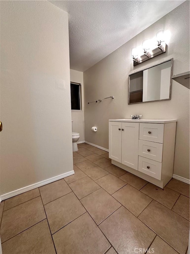 bathroom with tile patterned floors, toilet, a textured ceiling, baseboards, and vanity