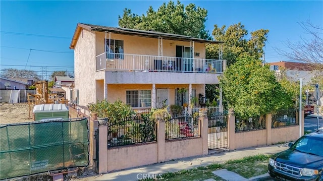 front of property with a gate, a fenced front yard, a balcony, and stucco siding