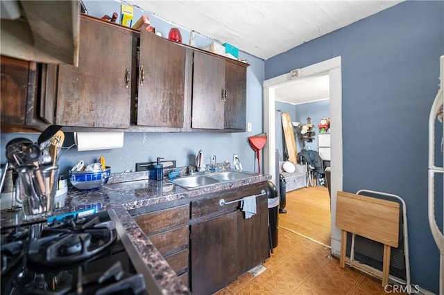 kitchen featuring dark countertops, dark brown cabinets, light floors, black gas cooktop, and a sink