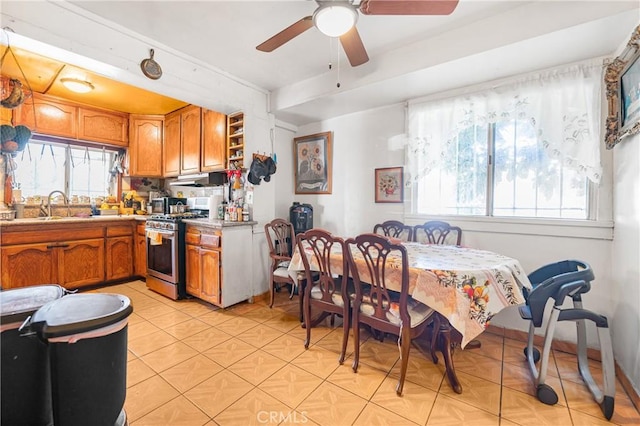 kitchen with stainless steel gas range oven, a sink, brown cabinetry, light countertops, and light tile patterned floors