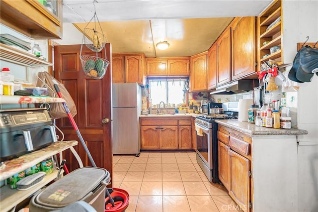 kitchen featuring a sink, under cabinet range hood, freestanding refrigerator, light countertops, and gas range