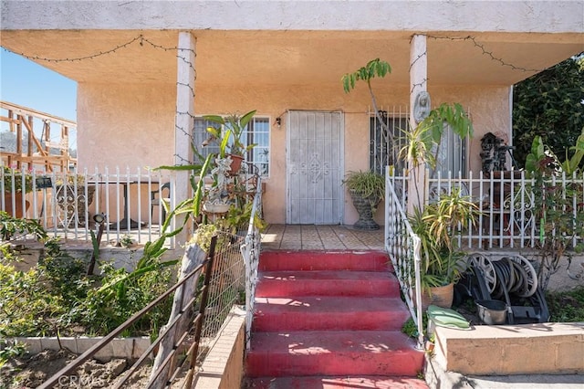 view of exterior entry featuring stucco siding and fence